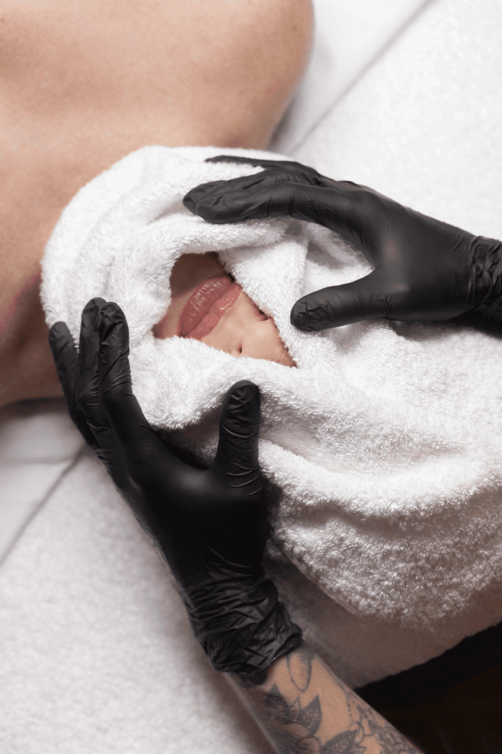 Facial massage with a warm towel by gloved hands in a spa setting.