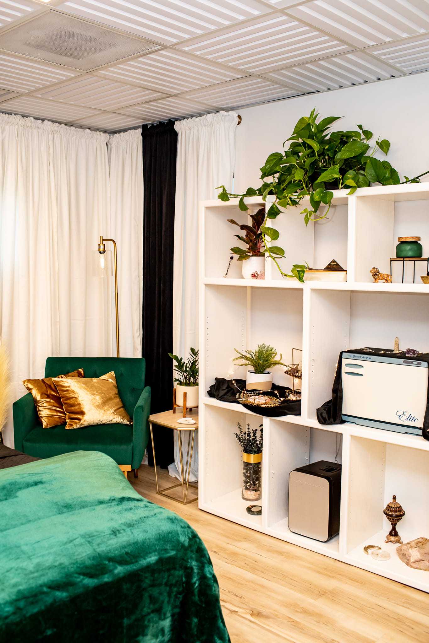 Cozy room with plants, white shelves, green chair, and gold-accented decor.