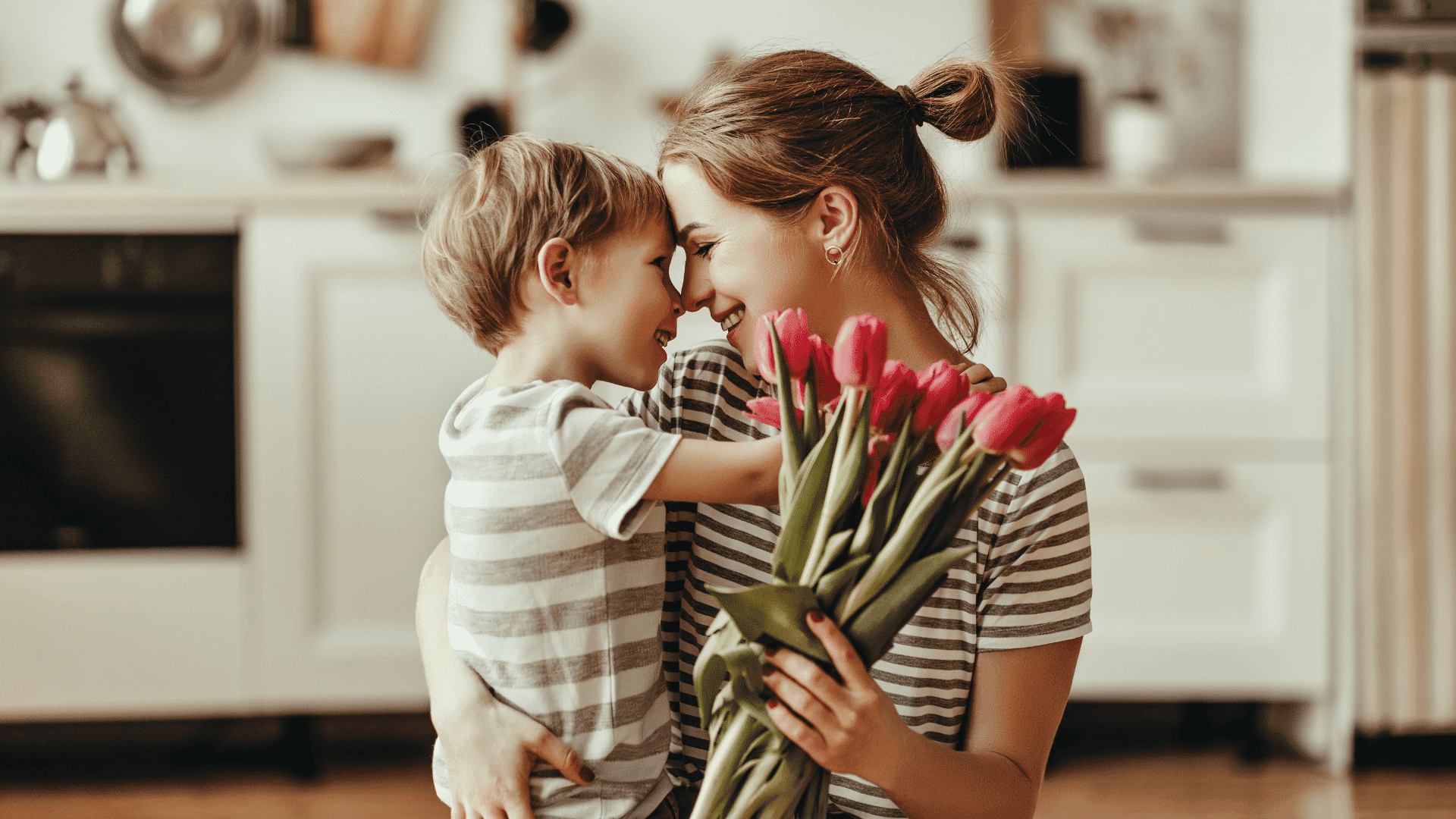 Mother and son smiling with a bouquet of tulips in a cozy kitchen.