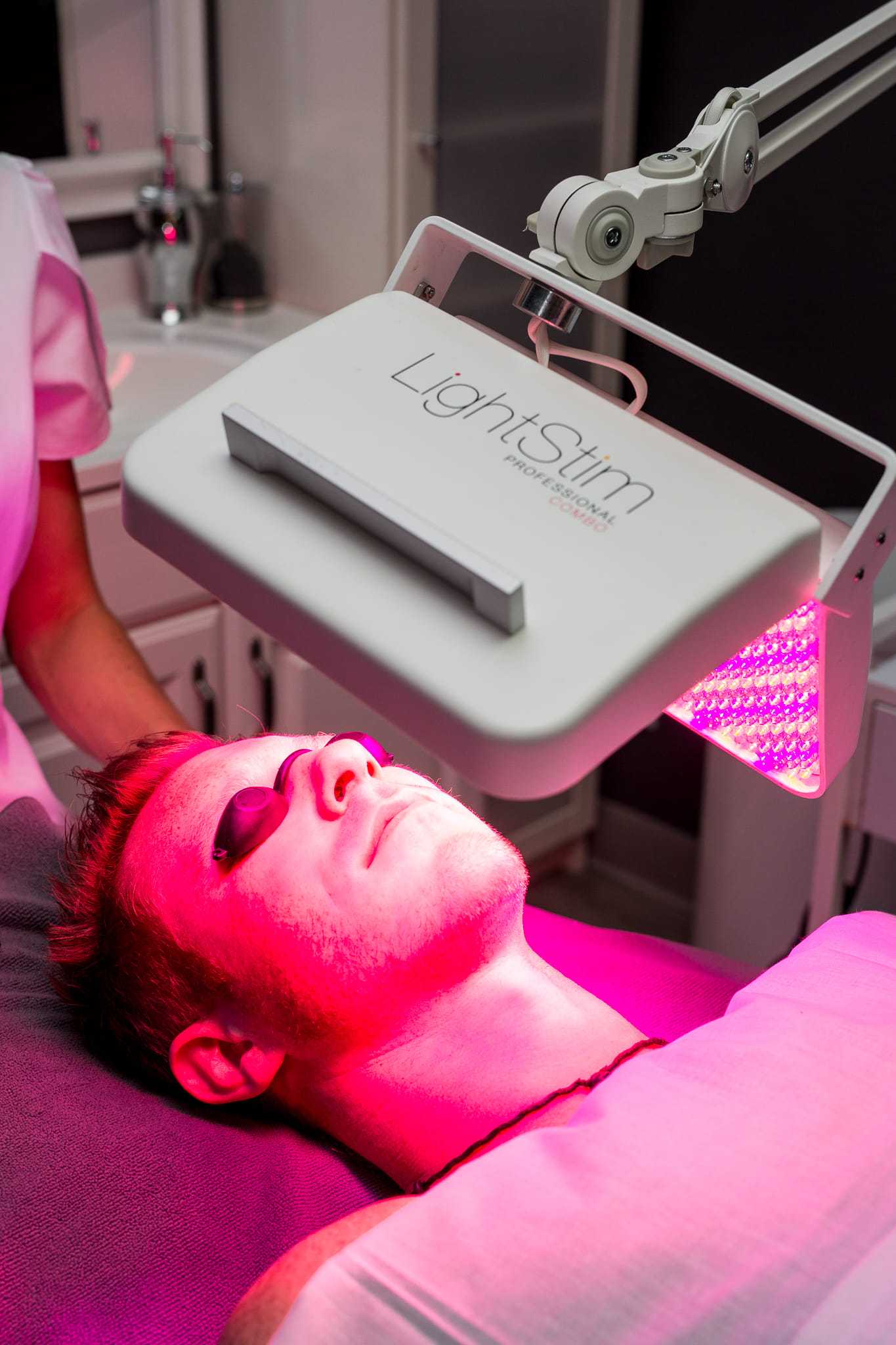 Man receiving LED light therapy facial treatment in spa setting.