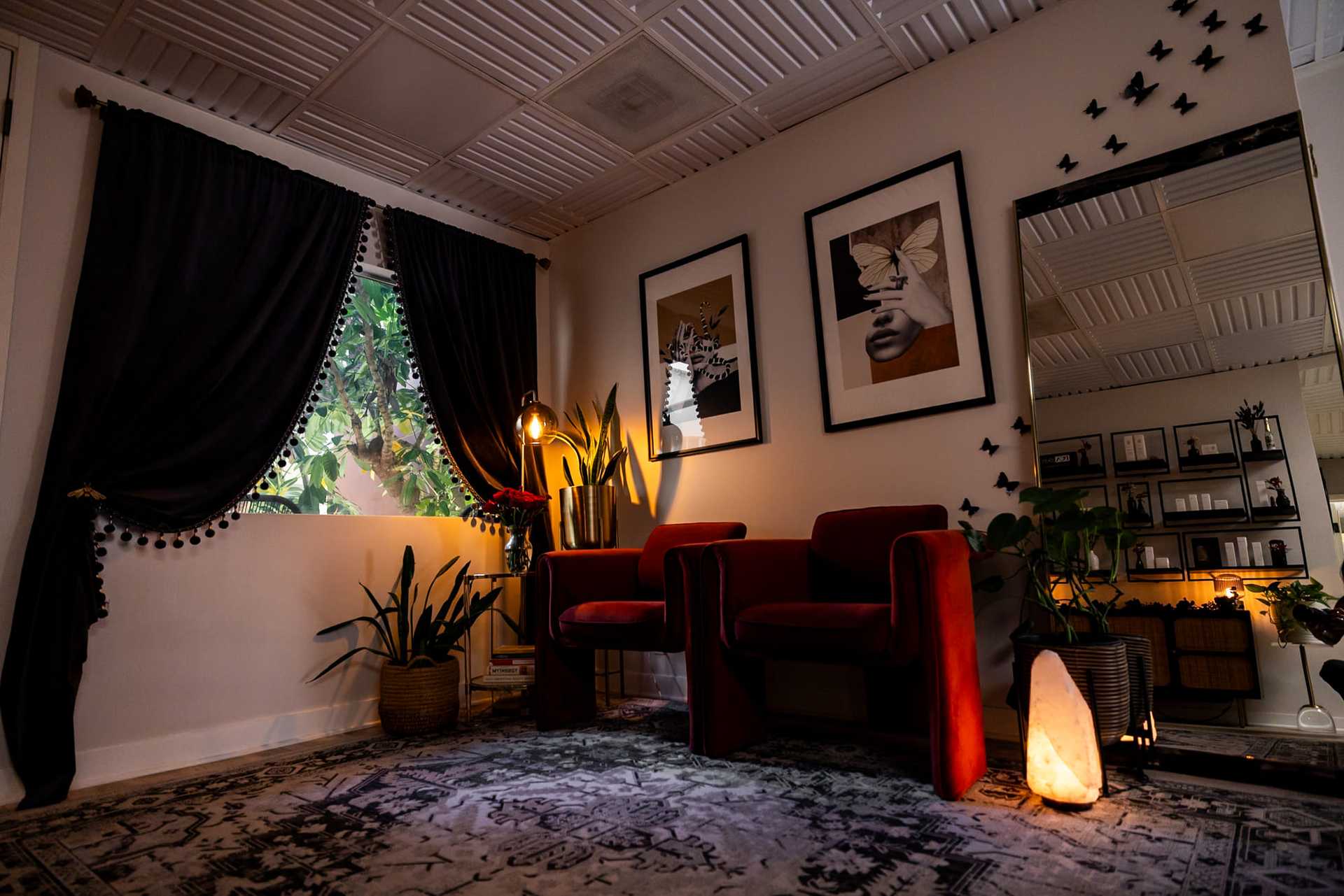 Cozy living room with red chairs, plants, framed art, and warm lighting.
