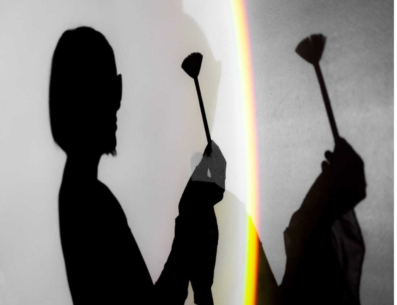 Shadow of a person holding an object, light rainbow effect on a white and gray background.