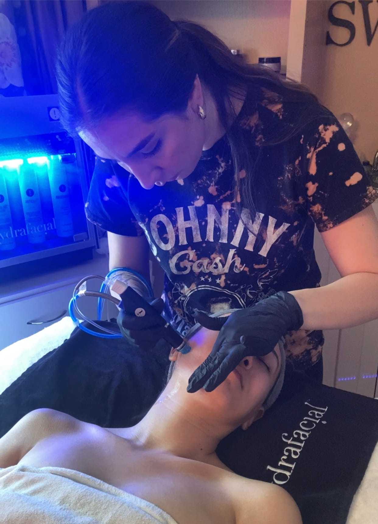 Esthetician performing a facial treatment on a reclining client in a spa setting.