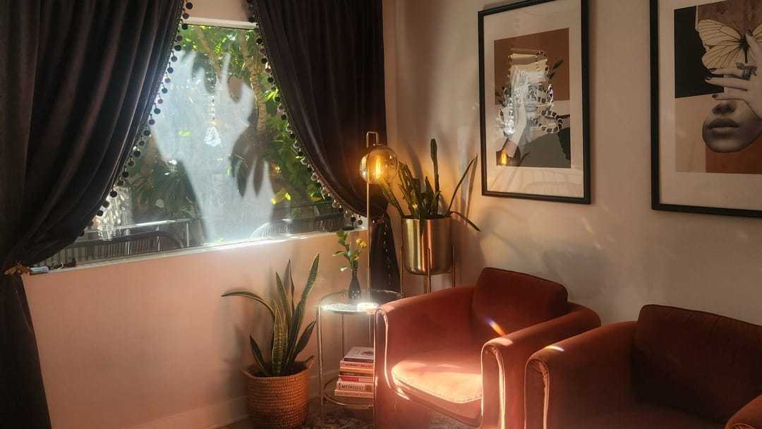 Cozy room with plants, two velvet chairs, and wall art bathed in warm sunlight.